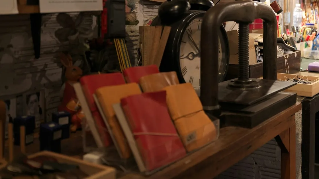 Mesa de taller de encuadernación con una prensa de husillo de hierro y varios libros cosidos a mano con cubiertas blandas de cuero